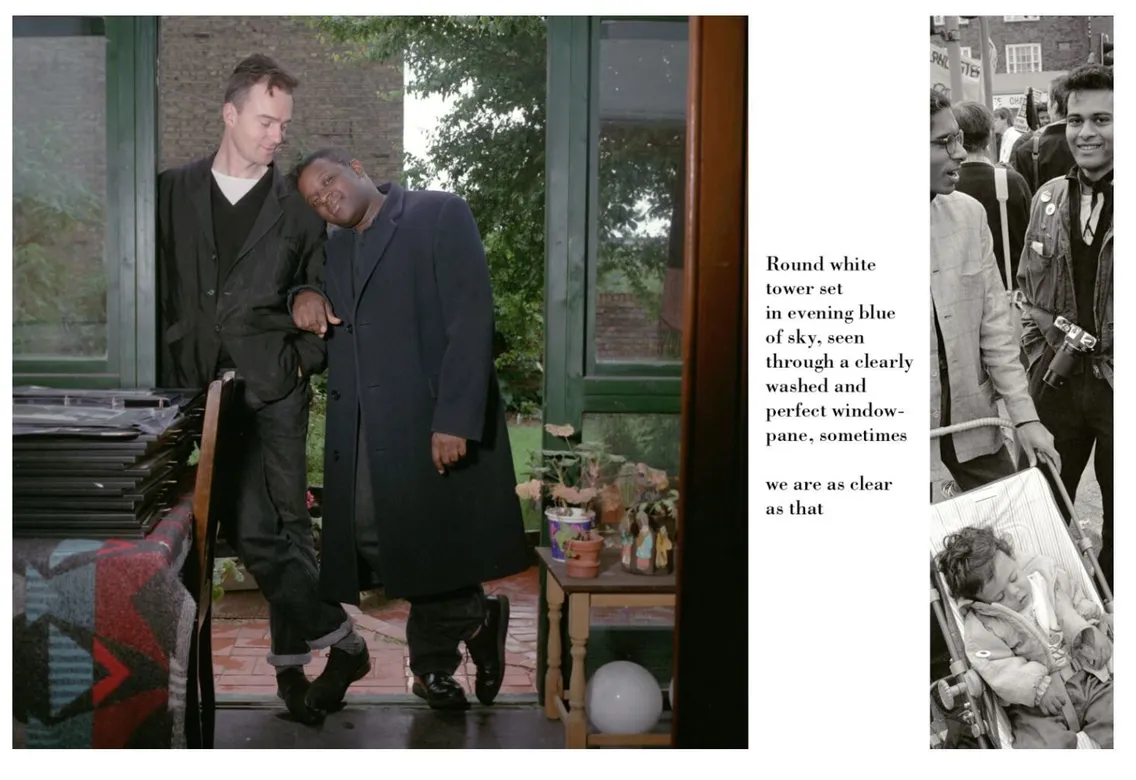 Two men, one leaning affectionately on the other by a window, in a room filled with records and books.