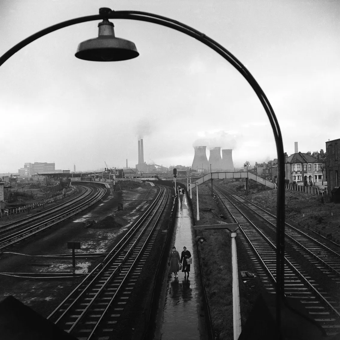 Black and white photo of seven smiling schoolchildren playfully peeking through metal bars.