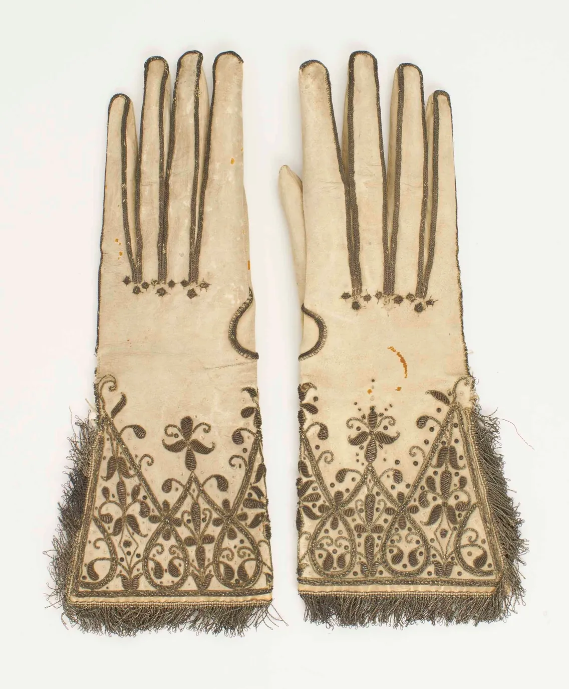 White gloves embroidered with silver thread forming plants, leaves and flowers.