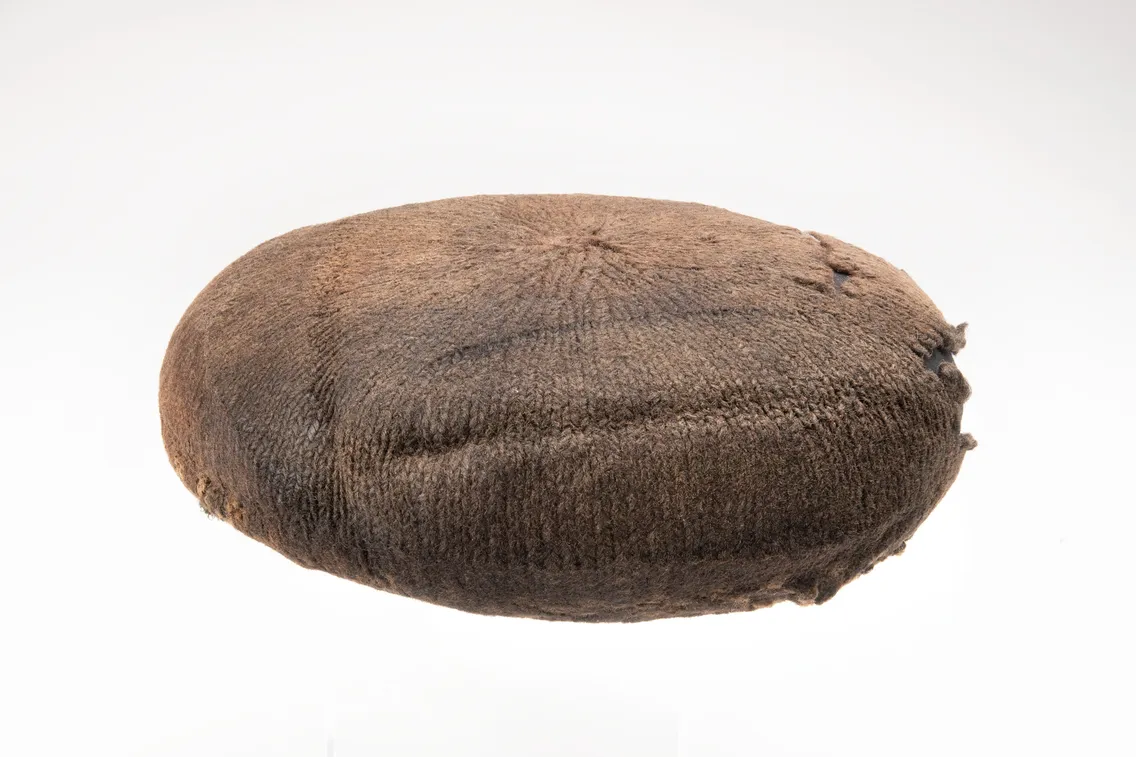A round, brown, flat woolen object resembling a traditional knit hat or cap against a plain white background.